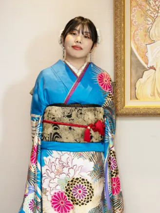 出雲・米子の成人振袖のレンタル・青を基調とした個性的な柄の振袖を着て、美術品のような背景に立つ女性。