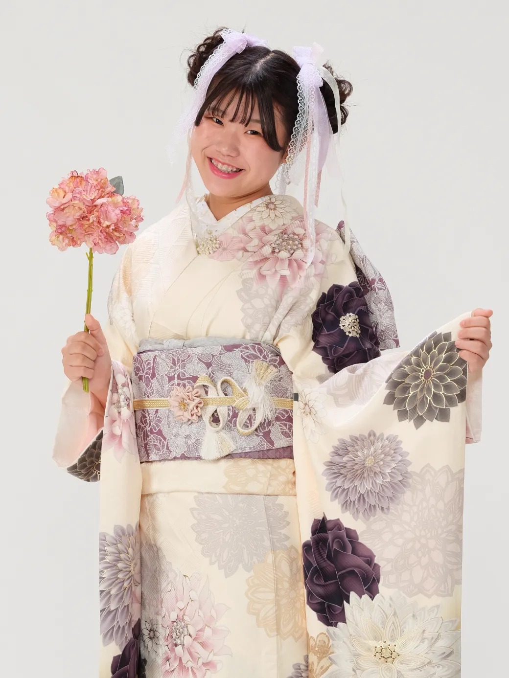 出雲・米子の成人振袖のレンタル・クリーム色に大きな花の柄が描かれた振袖を着て、花を持って微笑む女性。POPスタイル。