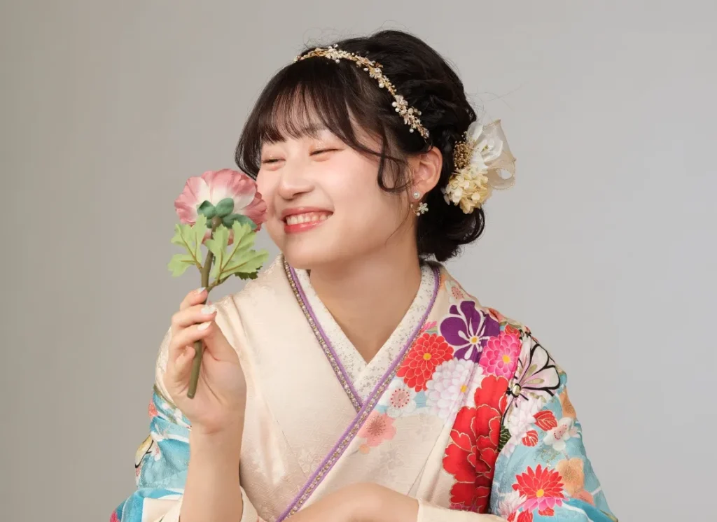 出雲・米子の成人振袖・成人袴のレンタル・白い振袖をまとい、花を持って微笑む女性のポートレート。創業98年の老舗による安心感を伝える画像。